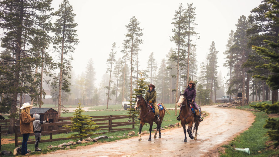 Two women riding horses together in the rain.