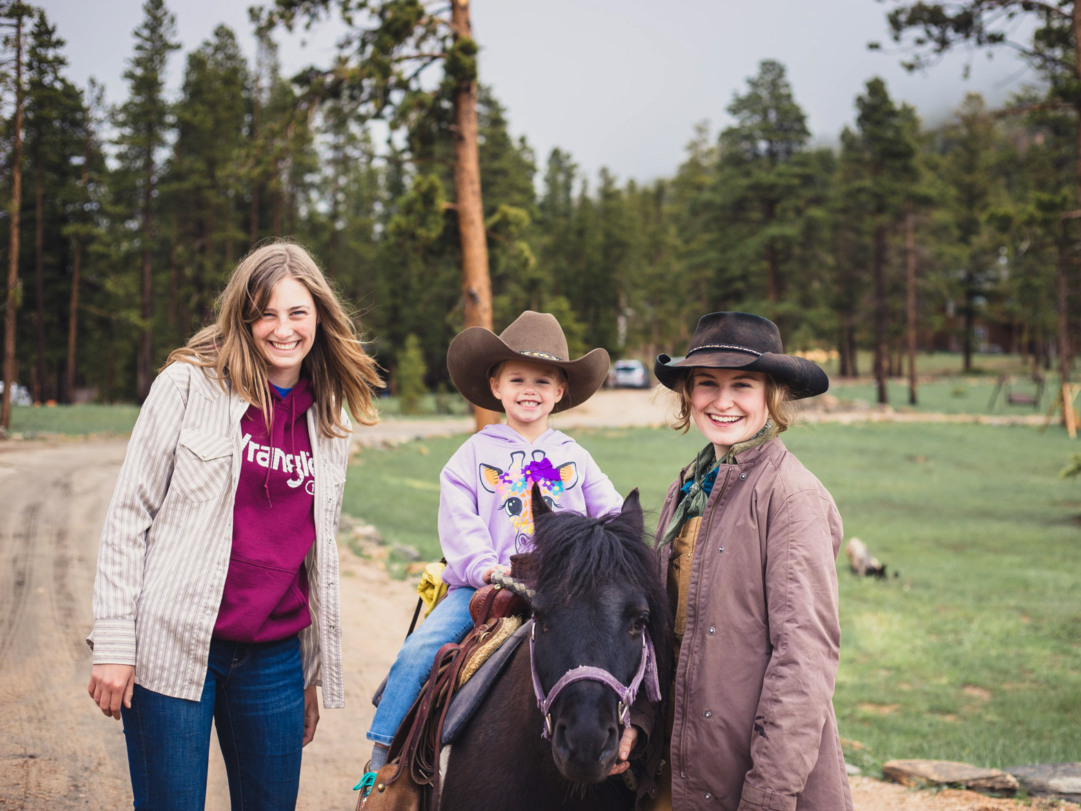 A little girl riding a horse with two young women helping her by her side.